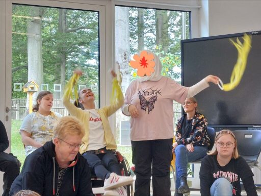 Jugendliche in einem Raum, einige mit bunten Tüchern, die aktiv an einer Aktivität teilnehmen.