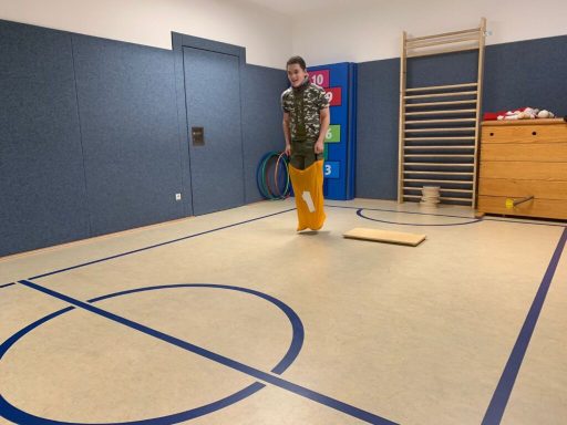 Junger Mann in farbenfroher Kleidung steht in einem Sportraum auf einem Holzbrett.