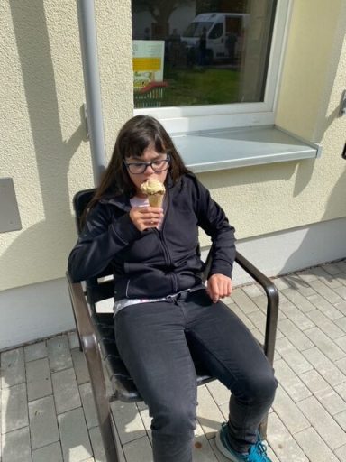 Person in schwarzer Jacke sitzt auf einem Stuhl und genießt ein Eis.