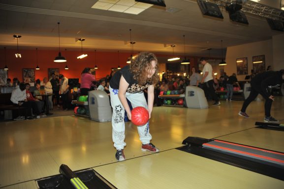 Eine Person mit lockigem Haar bereitet sich darauf vor, eine Bowlingkugel zu werfen.