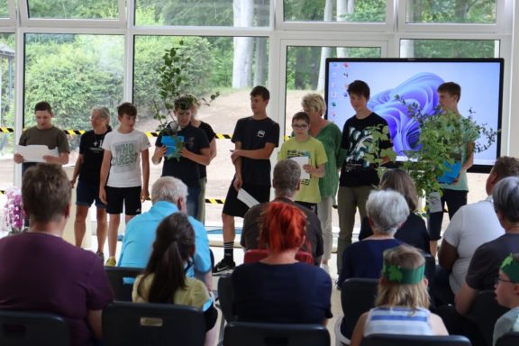 Kinder präsentieren eine Aufführung vor Publikum in einem hellen Raum.