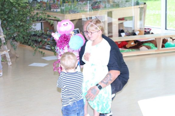 Eine Person mit kurzen, blonden Haaren umarmt ein Kleinkind mit einem Stofftier.