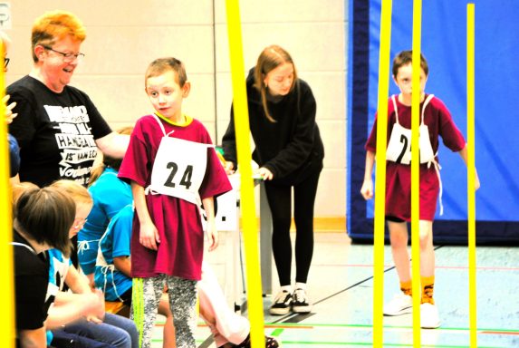 Zwei Kinder in Turnanzügen beim Wettbewerb, umgeben von Zuschauern und Betreuern.
