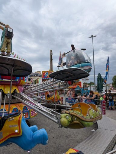Bunte Jahrmarktsattraktionen mit einem Karussell und Besuchern unter bewölktem Himmel.
