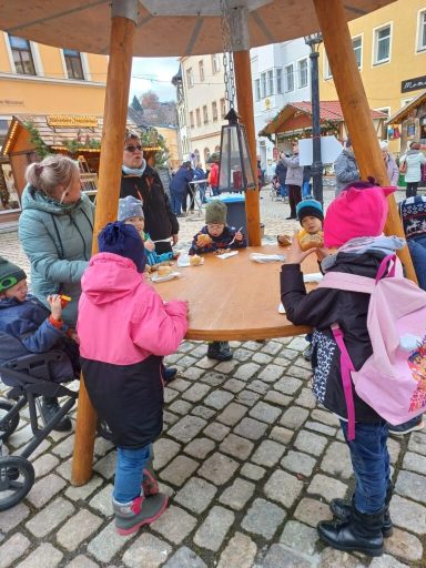 Eine Gruppe von Kindern spielt und bastelt an einem Tisch auf einem Platz.