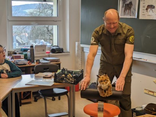 Ein Mann in Uniform steht vor Kindern und zeigt einen kleinen Tiger auf einem Stuhl.