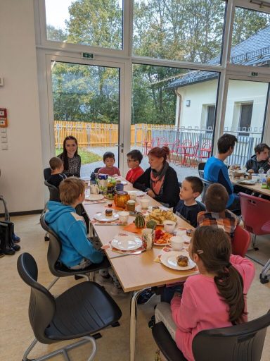 Gruppe von Kindern und Erwachsenen beim gemeinsamen Essen in einem hellen Raum.