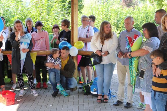 Menschen versammeln sich feierlich unter einem überdachten Bereich, Dekorationen im Hintergrund.