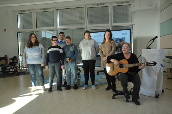 Gruppe von sieben Personen, die gemeinsam in einem Raum stehen und eine Gitarre halten.