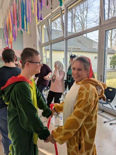 Zwei Personen in Kostümen, ein Dinosaurier und eine Giraffe, bei einer Feier.