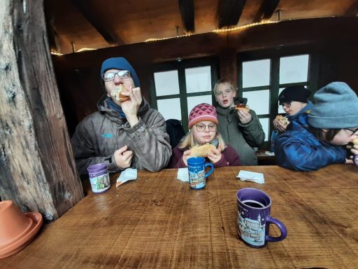 Fünf Personen sitzen an einem Holztisch mit bunten Tassen und lachen.