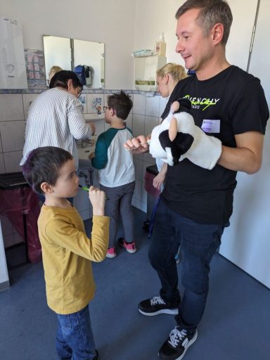 Ein Erwachsener interagiert spielerisch mit einem Kind, während andere im Hintergrund arbeiten.