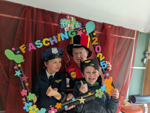 Drei Kinder in Kostümen mit einem bunten Faschingsrahmen.