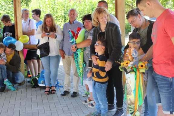 Gruppenszene mit Menschen, die an einer Feier stehen, einige halten Luftballons und Bänder.