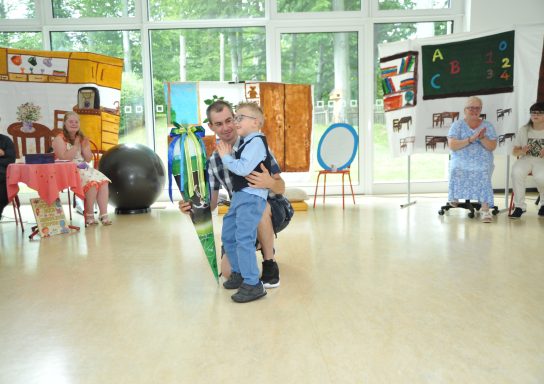 Ein Erwachsener hebt ein Kind in einer festlichen Umgebung mit Publikum.