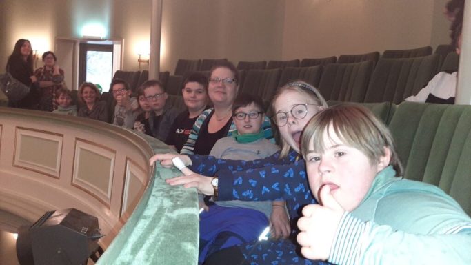 Eine Gruppe von Menschen, darunter Kinder, sitzt im Publikum eines Theaters.