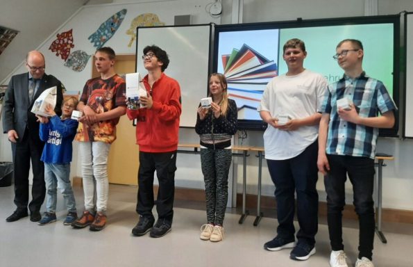 Sechs Personen stehen vor einem Bildschirm und halten Bücher in den Händen.