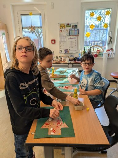 Drei Kinder basteln an einem Tisch mit Materialien und Dekorationen.