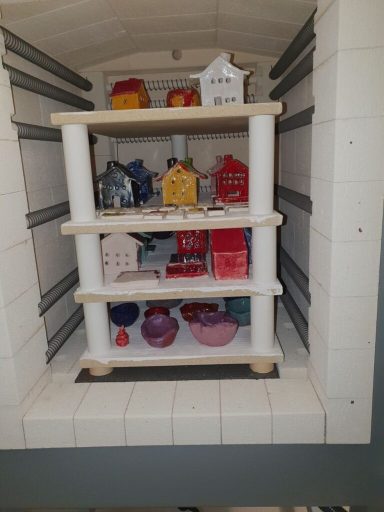 Blick in einen Ofen mit mehreren Regalen voller farbiger Keramikobjekte.