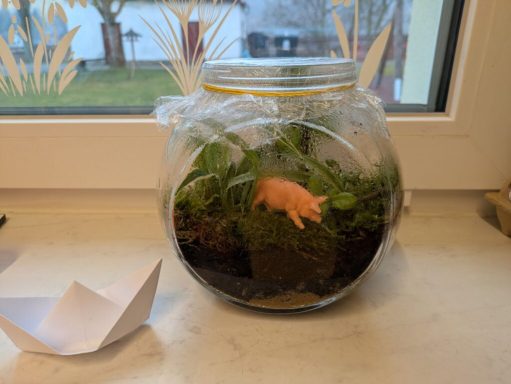 Ein Glasgefäß mit Moos und einer kleinen Plastikfigur eines Piggeldy.