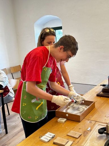 Zwei Personen arbeiten gemeinsam an einem Tisch, während sie etwas in einer Kiste inspizieren.