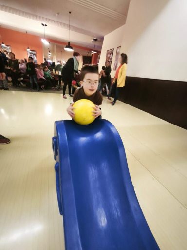 Ein Kind spielt mit einem gelben Ball auf einer blauen Rutsche in einem Spielraum.