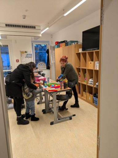 Drei Personen arbeiten an Tischen in einem hellen, modernen Raum mit Spielmaterialien.