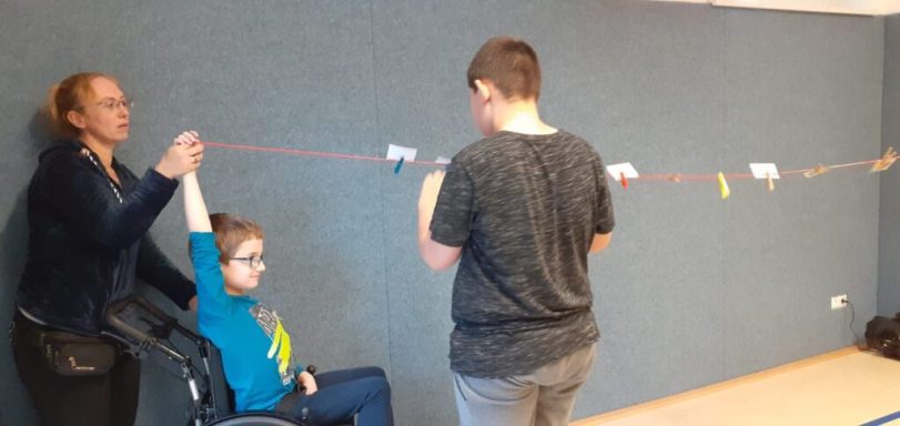 Eine Frau hilft einem Kind im Rollstuhl, während ein Junge eine Schnur hält.