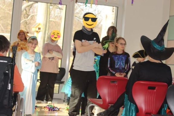 Kinder und Erwachsene in Kostümen feiern eine Veranstaltung mit fröhlichen Emojis.