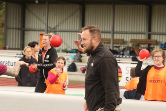 Sportveranstaltung mit mehreren Teilnehmern, die im Hintergrund Bälle werfen.