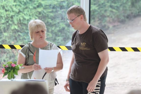 Zwei Frauen stehen nebeneinander, eine liest von einem Blatt Papier vor.