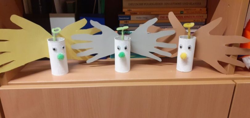 Bunte Pappen in Handform um weiße, dekorierte Rollen mit Gesichtern angeordnet.