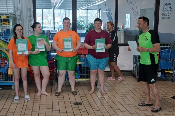 Fünf Personen in Badesachen halten Zertifikate in einer Schwimmhalle.