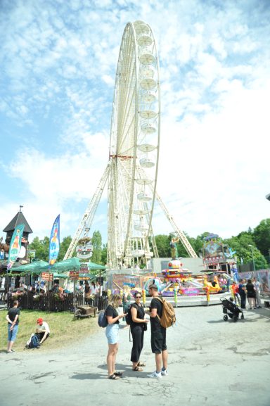 Gruppierung von drei Personen vor einem riesigen Riesenrad auf einem Festplatz.