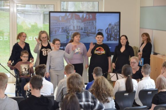 Gruppenszene mit Vortragenden und Publikum in einem modernen Raum.