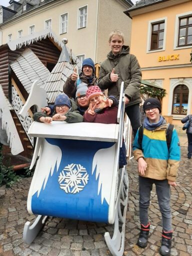 Sechs Personen stehen auf einer dekorierten Holzschlittenkonstruktion in einer Stadt.