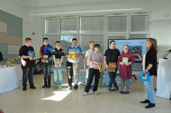 Gruppe von Jugendlichen steht in einem Raum und hält Bücher, während eine Person spricht.