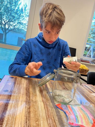 Junge in blauer Kapuzenjacke öffnet ein Glas auf einem Tisch.