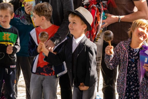 Kinder in bunten Kleidern halten Instrumente und feiern zusammen. Ein Junge trägt einen Hut.
