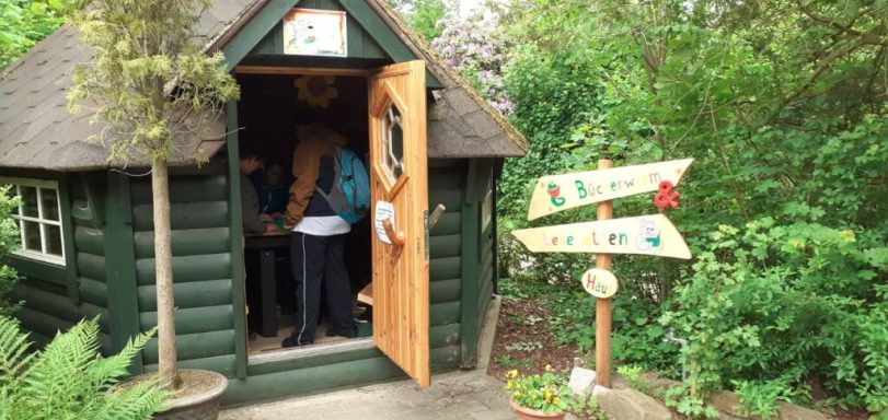 Ein grünes Gartenhaus mit offener Tür und Wegweisern im Vordergrund.