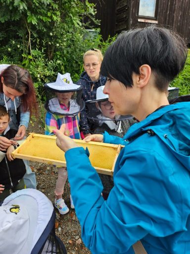 Eine Frau zeigt eine Honigwabe einer Gruppe von Kindern und Erwachsenen.
