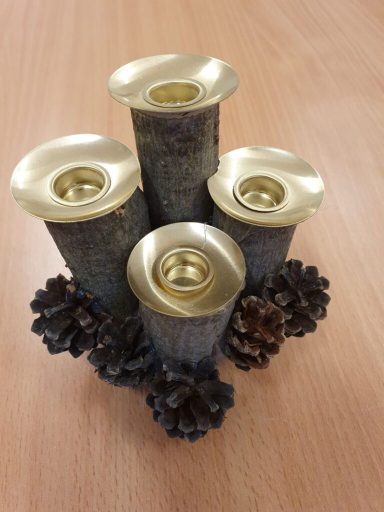 Vier Kerzenhalter aus dunklem Metall mit goldenen Öffnungen, umgeben von Tannenzapfen.