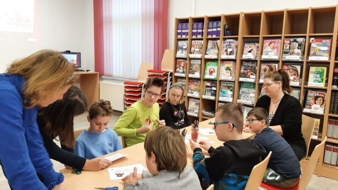 Gruppe von Kindern und Erwachsenen, die an einem Tisch in einem Raum arbeiten.