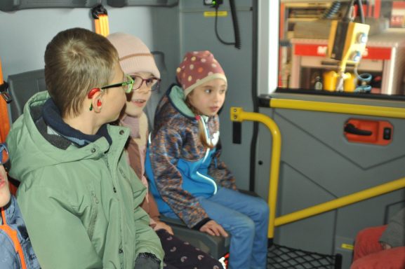Drei Kinder sitzen in einem Fahrzeug und schauen neugierig nach draußen.