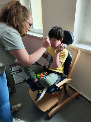 Ein Junge sitzt in einem Stuhl, während ein Mädchen ihm etwas füttert.