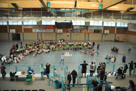 Gruppensitzung in einer Sporthalle mit zahlreichen Teilnehmern auf dem Boden.
