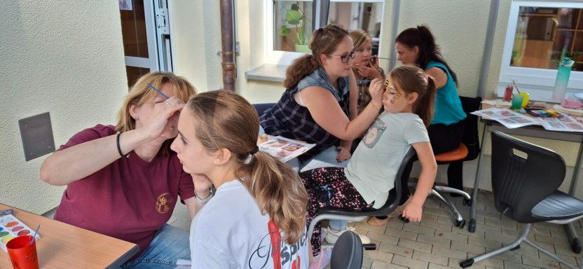 Mehrere Personen, darunter Kinder, spielen und malen gemeinsam in einem Raum.