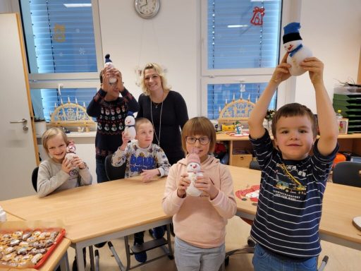 Sechs Kinder und zwei Erwachsene halten selbstgemachte Schneemann-Figuren.