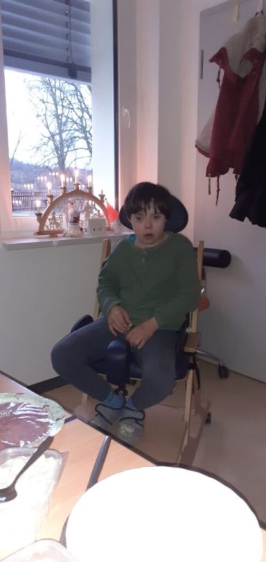 Ein Kind sitzt auf einem Stuhl in einem Raum mit einem Fenster und einem Tisch.