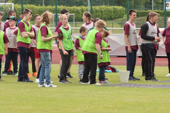 Gruppen von Kindern und Jugendlichen in grünen Westen auf einem Sportplatz.